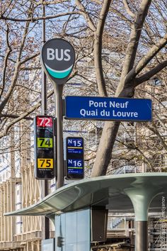 a bus station with gas pumps and signs on the side of the road in front of some trees