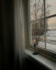 a candle is sitting on a window sill in front of the snow covered field