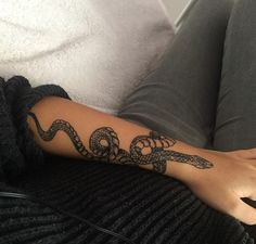 a woman's arm with a snake tattoo on it, sitting on a couch