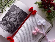 an open book with crocheted red and white bows on it next to flowers