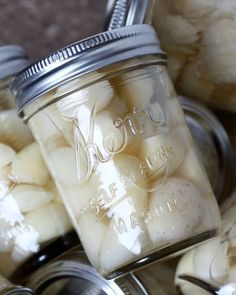 jars filled with white onions sitting on top of a counter next to garlic cloves