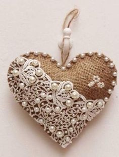 a heart shaped ornament with pearls and lace hanging from a string on a wall