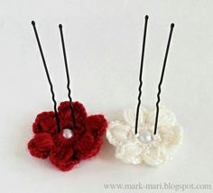 two crocheted flowers with black pins in them on a white surface, one is red and the other is white