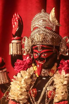 the statue is decorated with red and white flowers in front of a red curtained background