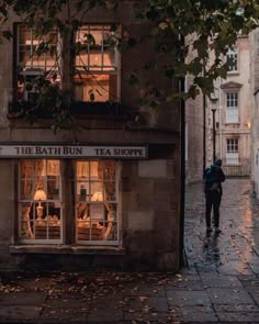 a man walking down the street in front of a tea shop on a rainy day