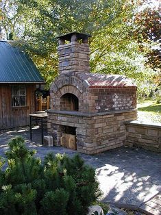 an outdoor brick pizza oven sitting on top of a stone patio next to a tree