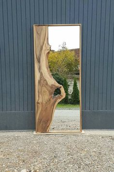 a large wooden mirror sitting on top of a gravel ground next to a building with a tree trunk sticking out of it's side