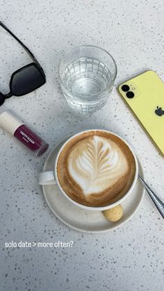 a cappuccino on a saucer next to an iphone, sunglasses and eyeglasses