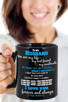 a woman holding up a black coffee mug with her husband's poem on it