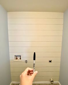 a person holding a pen in front of a wall with white planks on it