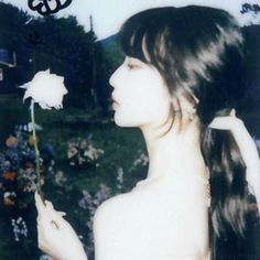 a woman with long hair holding a flower in her hand and looking at the camera