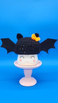 a knitted hat with bat wings and a yellow bow on top, sitting on a pedestal