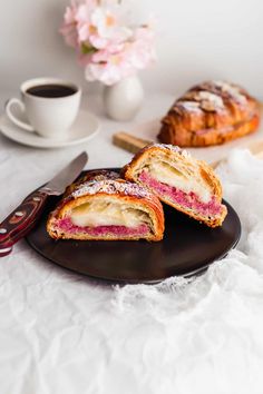 two pastries on a black plate next to a cup of coffee and spoons