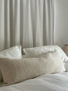 a white bed with two pillows on top of it next to a lamp and window