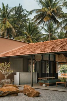 an outdoor area with rocks and trees in the foreground, near a building that has a red tiled roof