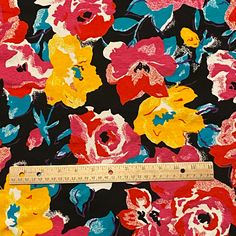 a ruler is next to a colorful flower print on a black background with red, yellow and blue flowers