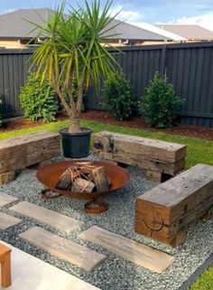 a fire pit surrounded by wooden benches in the middle of a yard with a potted plant