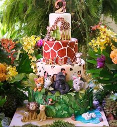 a three tiered cake with animals and plants around it on a table surrounded by flowers