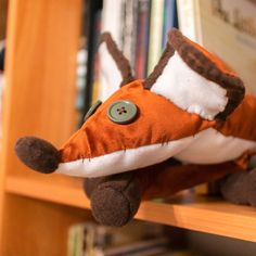 a stuffed animal that is laying down on a book shelf in front of a bookshelf