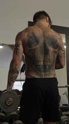 a man with tattoos on his back standing in front of a mirror and holding a barbell