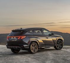 the rear end of a gray suv parked on top of a hill at sunset with mountains in the background