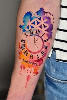 a watercolor style clock tattoo on the left forearm and arm with an ink splattered design