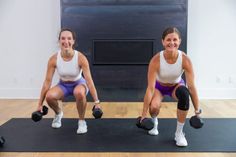 two women are doing squats with dumbbells in front of a fire place