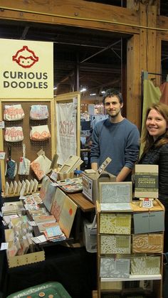 two people standing in front of a table full of cards and books at a booth