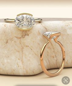 an engagement ring with two diamonds on it sitting on top of a marble block next to a stone slab