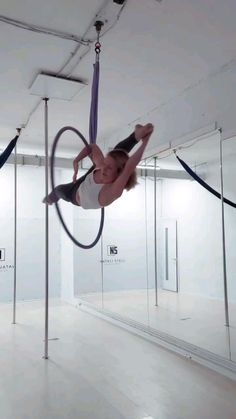 a woman is doing aerial tricks on a hoop in an empty room with glass walls