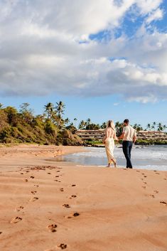 a man and woman walking on the beach next to the ocean with footprints in the sand