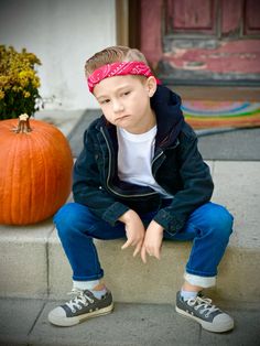 a young boy sitting on the steps next to a pumpkin