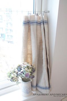 a vase with some flowers sitting on a window sill next to a curtained window