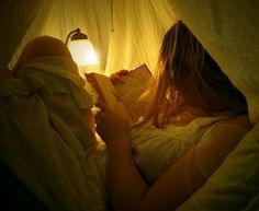 a woman is laying in bed reading a book at night time with the light turned on