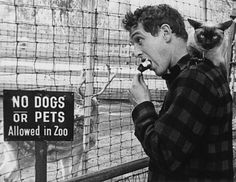 a man holding a cat while standing next to a sign that says no dogs or pets allowed in zoo