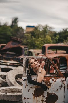 a woman leaning on the door of an old rusted out truck in a junkyard