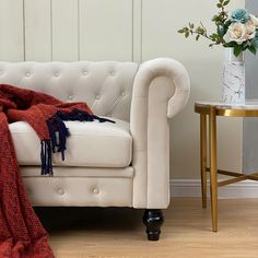 a white couch with a red blanket on it next to a small table and flowers