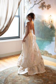 a woman standing in front of a window wearing a wedding dress and looking off to the side