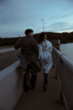 a man and woman walking across a bridge next to the ocean at dusk or dawn