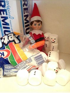 an elf is sitting next to some marshmallows and other items on the counter