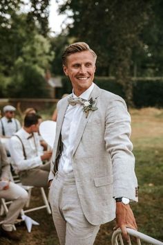 a man in a suit and bow tie standing next to other men wearing white suits