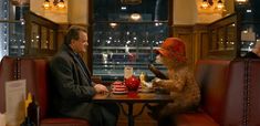 a man sitting at a table next to a brown bear