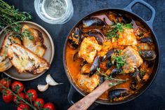 a pan filled with food next to some vegetables and bread on top of a table