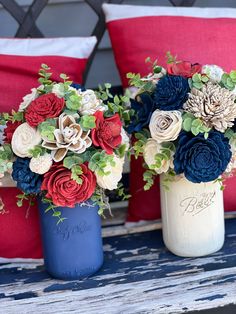 two vases with flowers are sitting on a bench next to red and white pillows