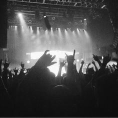 a crowd of people at a concert with their hands up in front of the stage lights