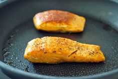 two pieces of salmon in a frying pan with seasonings on them and one piece being cooked