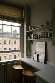 two wooden stools sit in front of a window with open shelves on each side