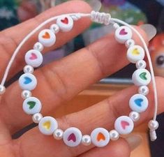 a hand holding a white bracelet with hearts and beads on the end, in front of a toy horse