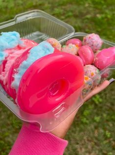 a plastic container filled with pink and blue doughnuts on top of green grass