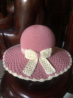 a pink crocheted hat with a bow on top sitting on a wooden chair